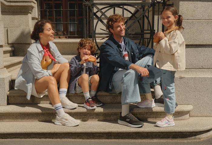Family of four sites on a couch before a dark wooden wall/closet.